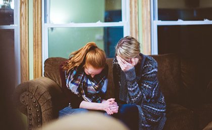 Two women sitting on a couch looking visibly upset